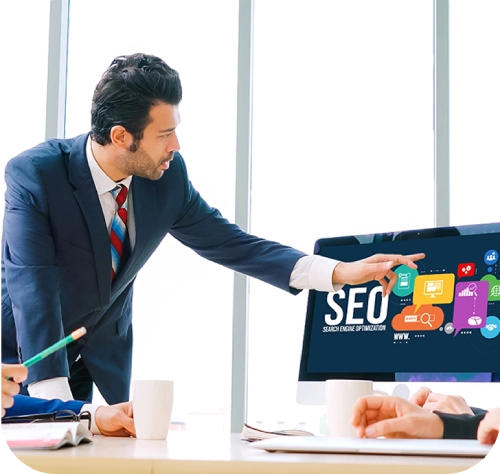 Professional in a suit pointing at a computer screen displaying 'SEO - Search Engine Optimisation' with icons representing analytics, websites, and search tools, highlighting expert local SEO services in a modern office setting on the Craze For Marketing Local SEO service page.
